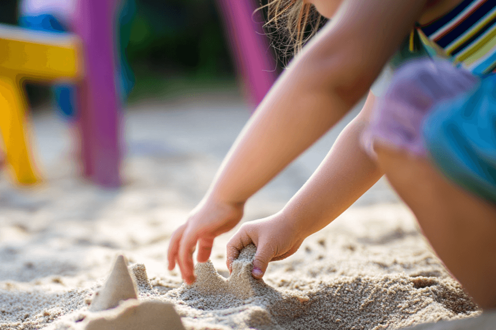 Ein kleines Mädchen spielt mit ihren Händen im Sand und baut eine Sandburg.